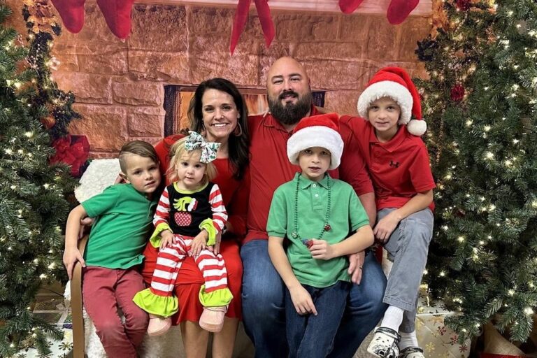 Brett McIntyre smiling with his wife Alicia and their four children in a Christmas setting, featured honoree family for Helping One Guy event.